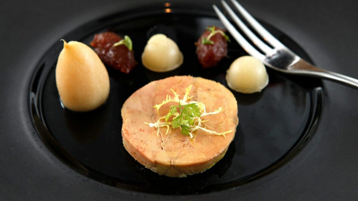 Delicate foie gras served on a black ceramic plate with garnish and puree accompaniments.