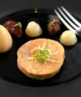 Delicate foie gras served on a black ceramic plate with garnish and puree accompaniments.