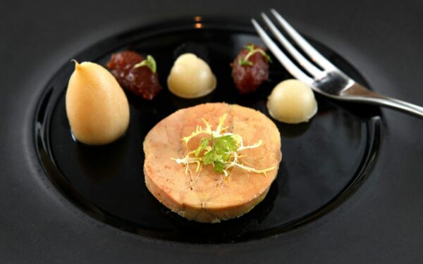 Delicate foie gras served on a black ceramic plate with garnish and puree accompaniments.