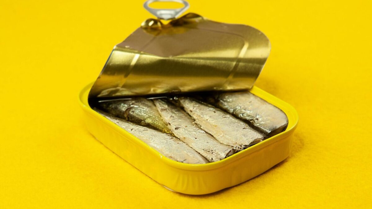 Close-up of an open sardine can on a vibrant yellow background, suitable for ads.