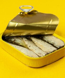 Close-up of an open sardine can on a vibrant yellow background, suitable for ads.