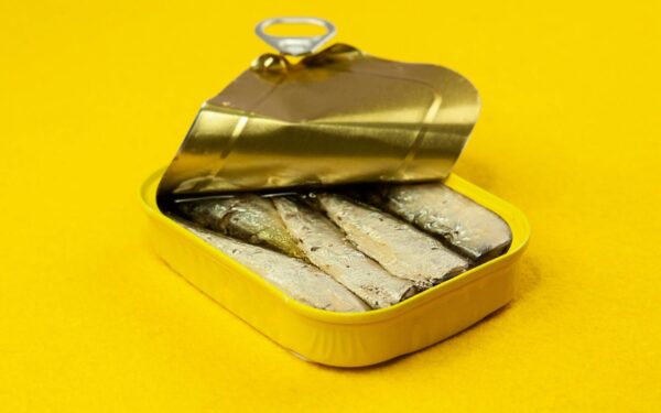 Close-up of an open sardine can on a vibrant yellow background, suitable for ads.