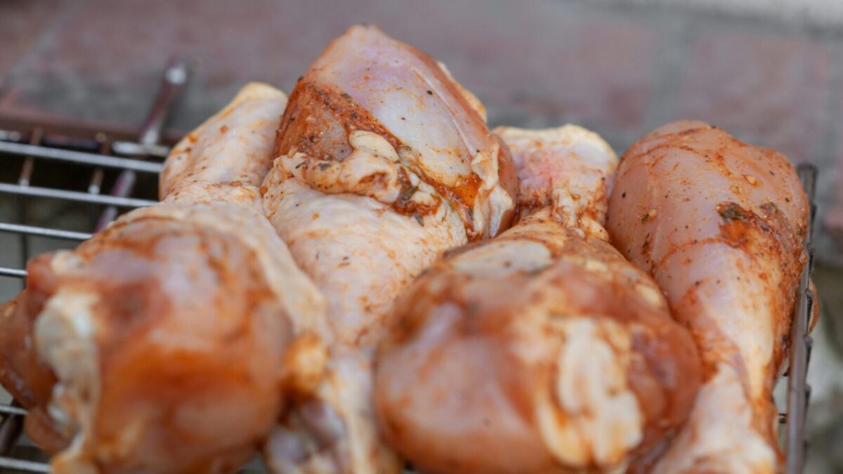 From above of raw chicken legs with seasoning placed on metal grill grate in daylight