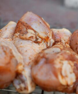 From above of raw chicken legs with seasoning placed on metal grill grate in daylight