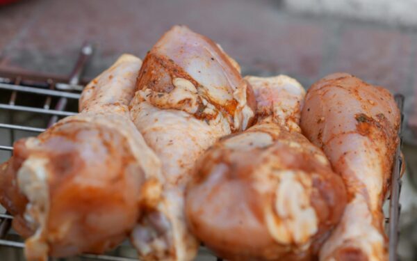 From above of raw chicken legs with seasoning placed on metal grill grate in daylight
