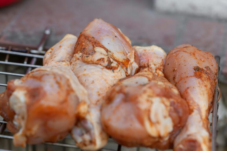 From above of raw chicken legs with seasoning placed on metal grill grate in daylight