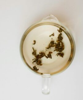 Top-down view of transparent cup with loose tea leaves on white background, offering ample copy space.