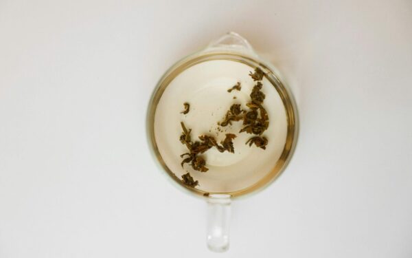 Top-down view of transparent cup with loose tea leaves on white background, offering ample copy space.