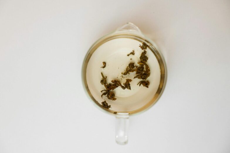 Top-down view of transparent cup with loose tea leaves on white background, offering ample copy space.
