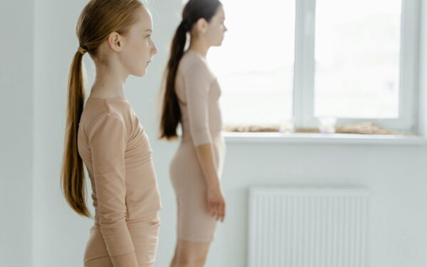 Two young ballerinas practicing posture in a ballet studio with graceful concentration.