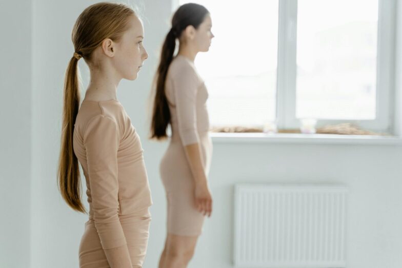 Two young ballerinas practicing posture in a ballet studio with graceful concentration.