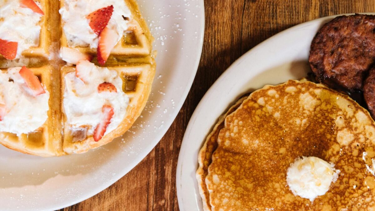 Enjoy a classic American breakfast featuring pancakes, waffles, and sausages topped with whipped cream and strawberries.