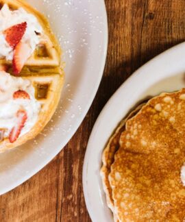 Enjoy a classic American breakfast featuring pancakes, waffles, and sausages topped with whipped cream and strawberries.