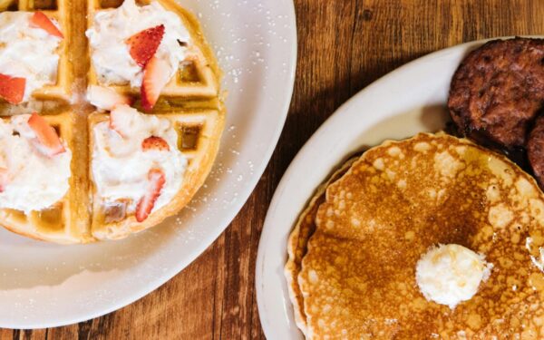 Enjoy a classic American breakfast featuring pancakes, waffles, and sausages topped with whipped cream and strawberries.