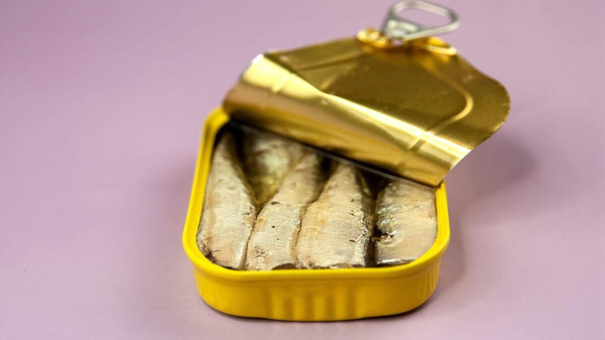 Closeup opened delicious canned fish with oil in yellow package placed on light purple background
