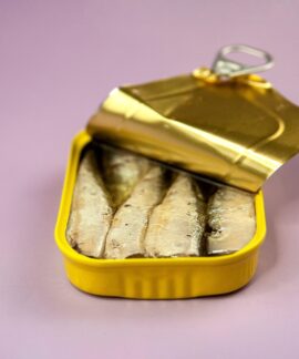 Closeup opened delicious canned fish with oil in yellow package placed on light purple background