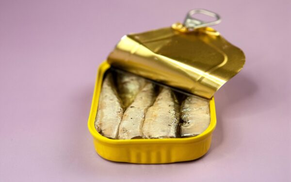 Closeup opened delicious canned fish with oil in yellow package placed on light purple background
