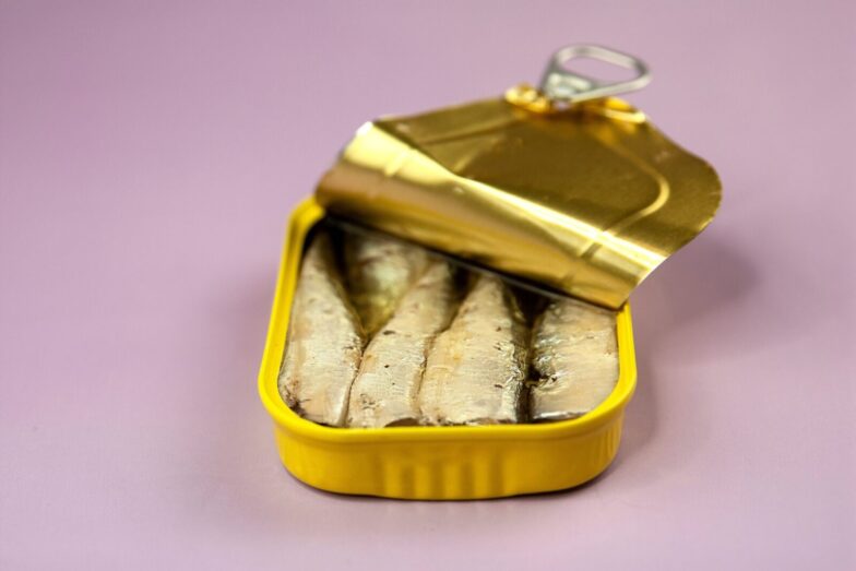Closeup opened delicious canned fish with oil in yellow package placed on light purple background