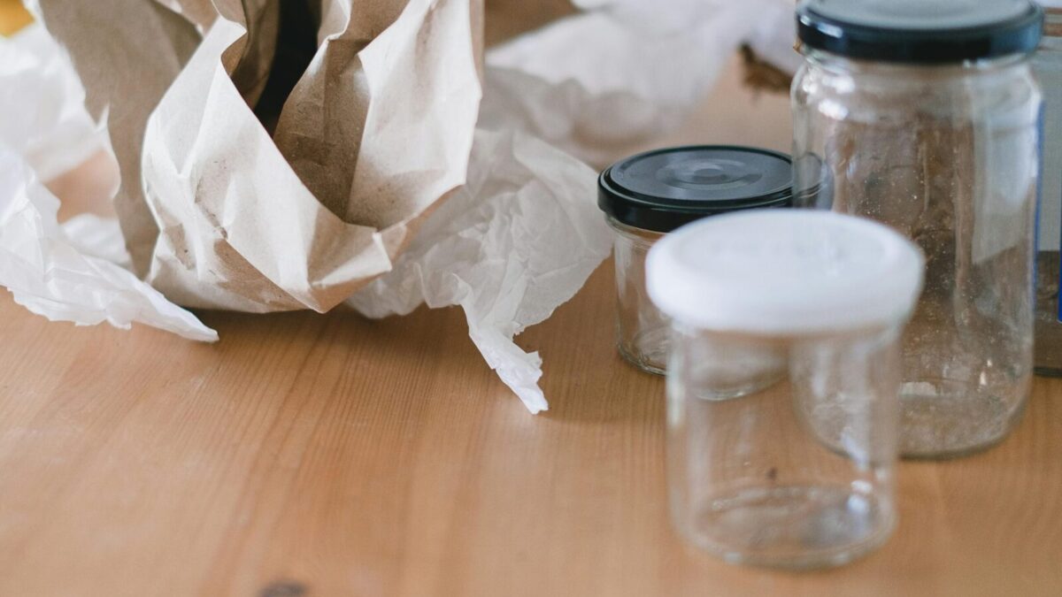 High angle of used empty glass jars with lids placed near creased paper for trash recycling