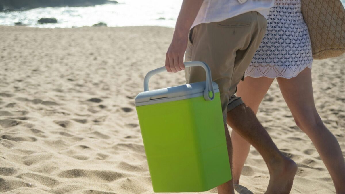 A couple walks along a sunny beach in Portugal carrying a cooler.