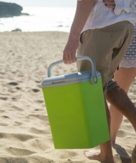 A couple walks along a sunny beach in Portugal carrying a cooler.