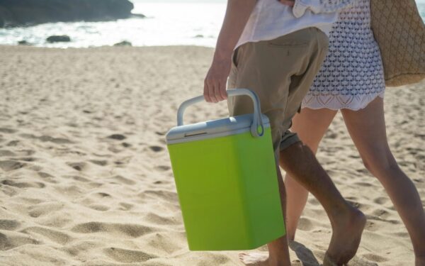 A couple walks along a sunny beach in Portugal carrying a cooler.