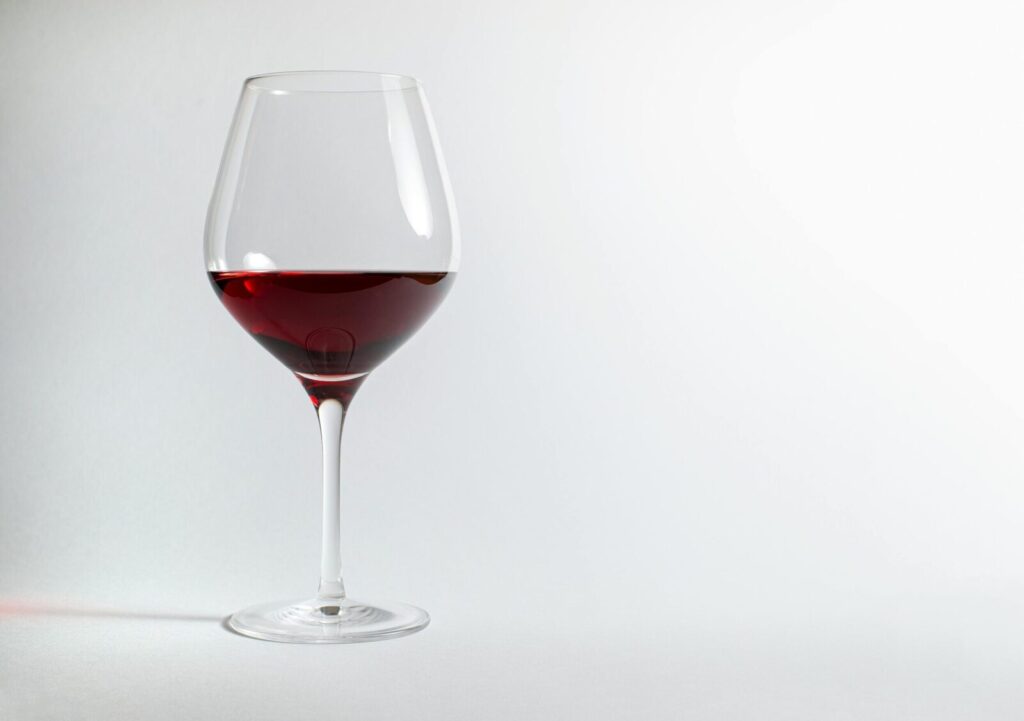 A half-filled glass of red wine on a plain white background perfect for design use.
