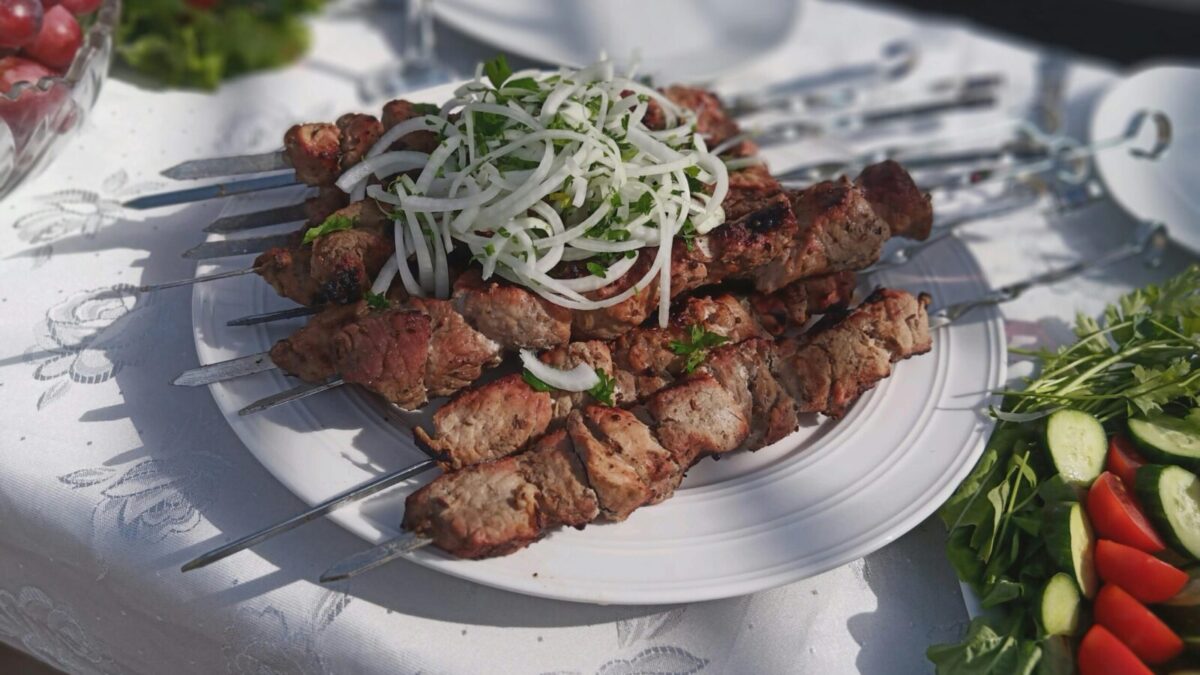 Delicious grilled meat skewers garnished with onions and fresh vegetables outdoors on a sunny day.