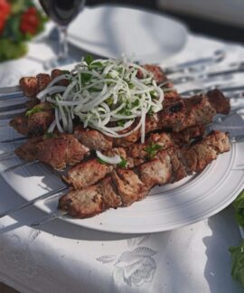 Delicious grilled meat skewers garnished with onions and fresh vegetables outdoors on a sunny day.