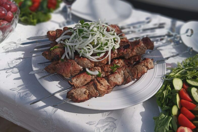Delicious grilled meat skewers garnished with onions and fresh vegetables outdoors on a sunny day.
