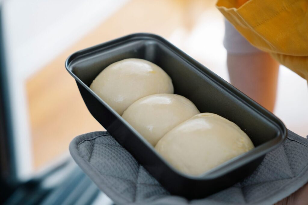 Close-up of dough balls in a baking tray held with an oven mitt, ready for baking.
