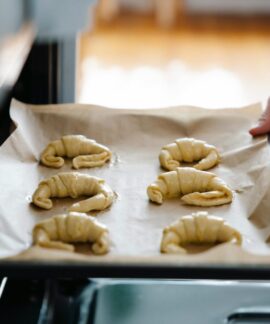 Hands placing homemade croissants on a tray into an oven, ready to bake.