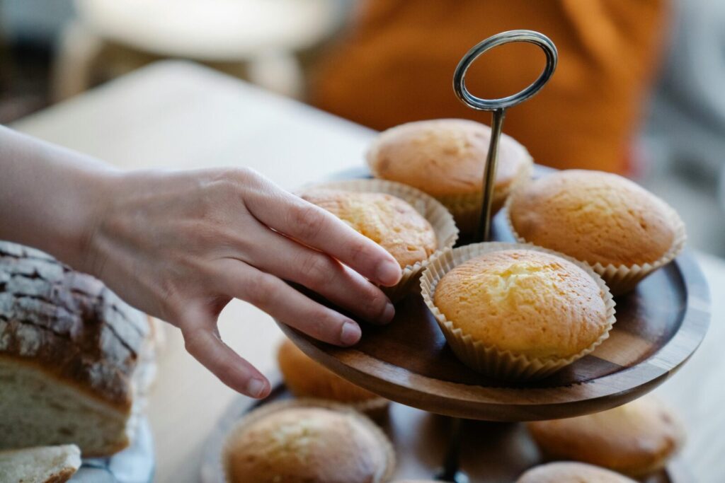 Close-up of a hand reaching for cupcakes on a wooden stand, indoors.