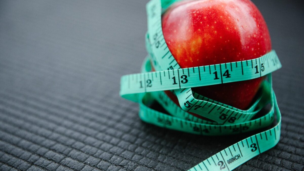 A vibrant red apple encircled by a blue measuring tape, symbolizing health and weight management.