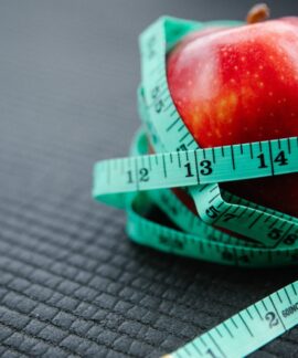 A vibrant red apple encircled by a blue measuring tape, symbolizing health and weight management.