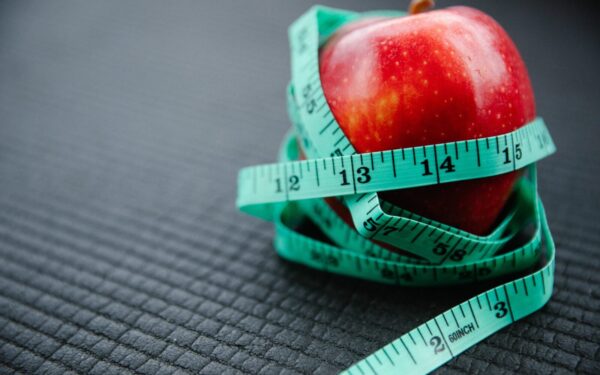 A vibrant red apple encircled by a blue measuring tape, symbolizing health and weight management.