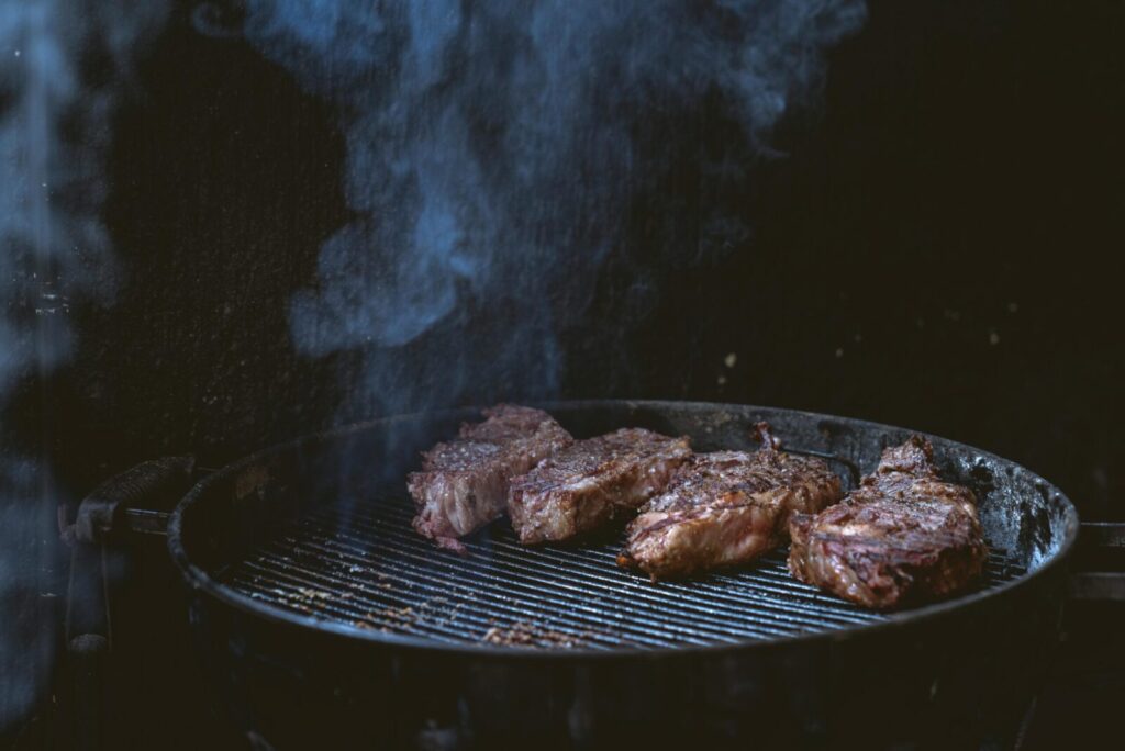 Close-up of juicy steaks grilling on a smoky barbecue, perfect for summer cookouts.