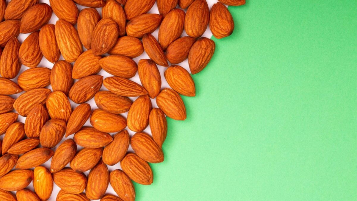 Close-up of organic almonds scattered on a green background, ideal for healthy eating concepts.