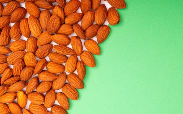 Close-up of organic almonds scattered on a green background, ideal for healthy eating concepts.