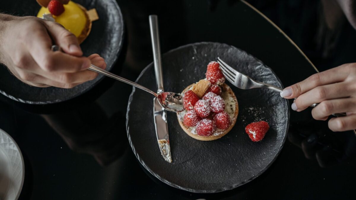 Close-up of a raspberry tart with powdered sugar on a black plate, top view.