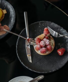Close-up of a raspberry tart with powdered sugar on a black plate, top view.