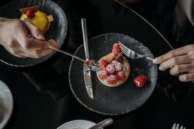 Close-up of a raspberry tart with powdered sugar on a black plate, top view.