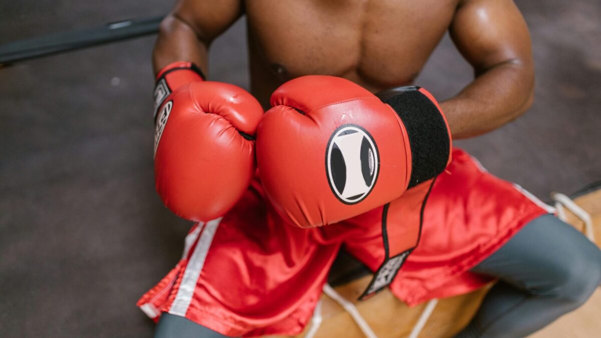 Shirtless boxer in red gloves and shorts preparing for a match in the gym.