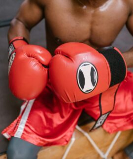 Shirtless boxer in red gloves and shorts preparing for a match in the gym.