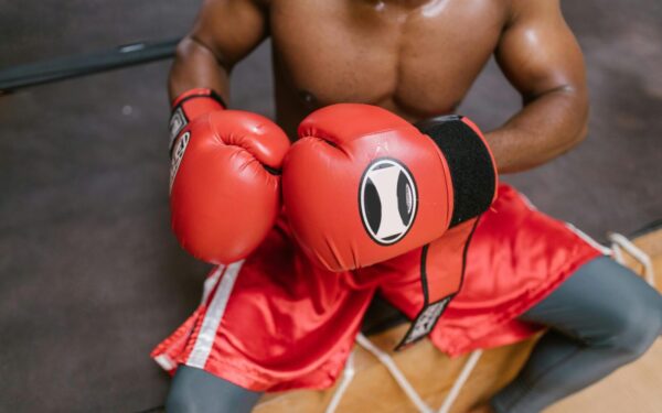 Shirtless boxer in red gloves and shorts preparing for a match in the gym.