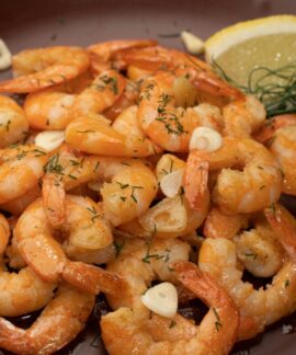 Close-up of flavorful shrimp garnished with garlic, lemon, and dill.