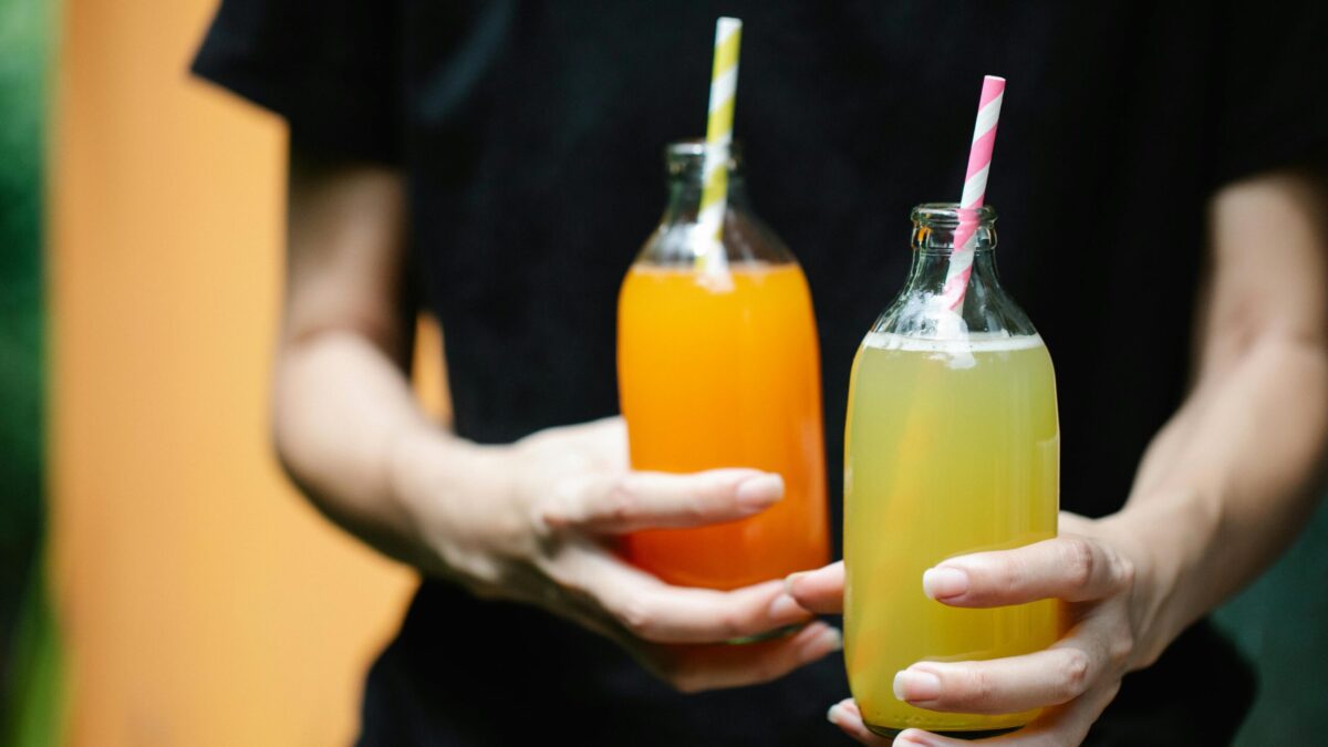 Two colorful juices in glass bottles with straws, perfect for summer refreshment.