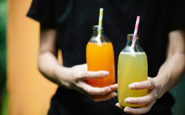 Two colorful juices in glass bottles with straws, perfect for summer refreshment.