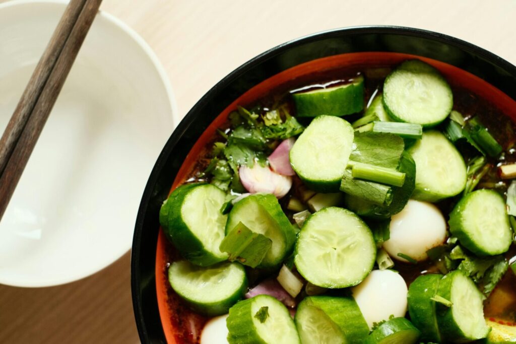 Top view of fresh vegetable soup with cucumber slices, herbs, and eggs in a bowl.