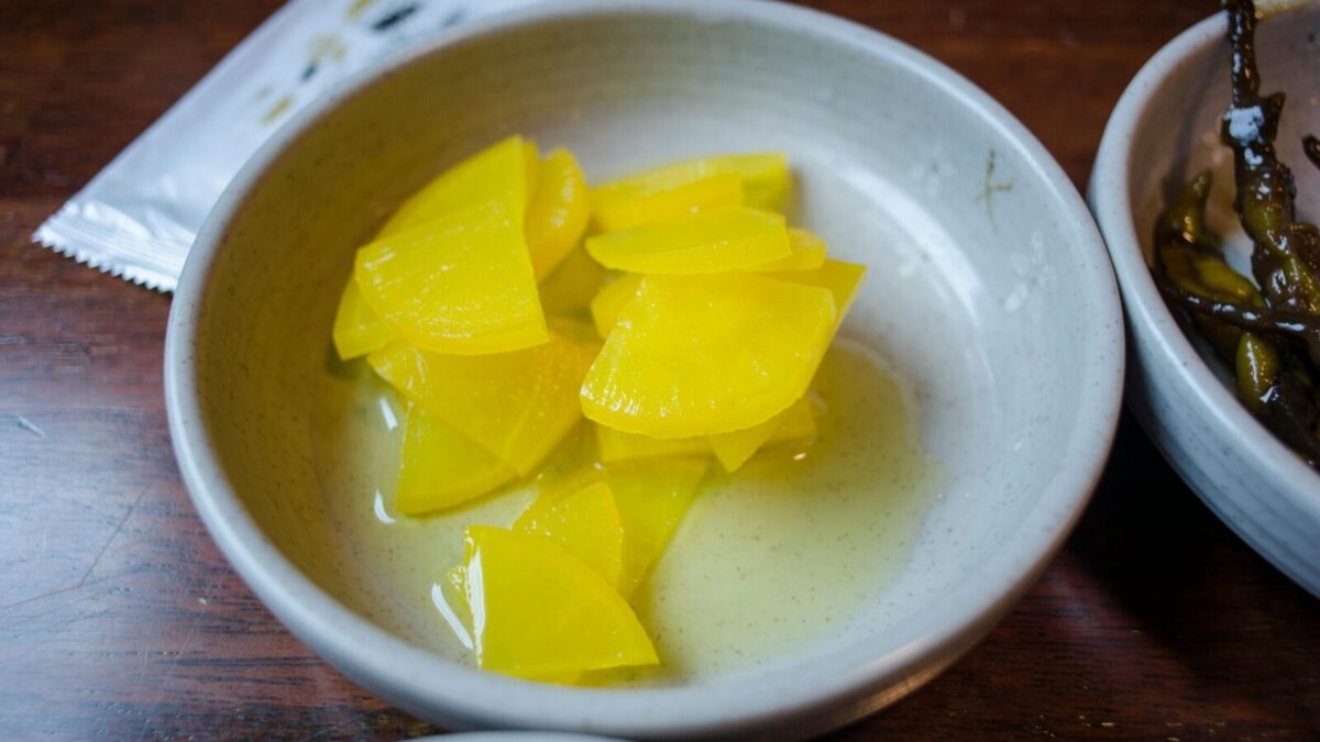 Close-up of sliced yellow pickled daikon radish in a ceramic bowl.